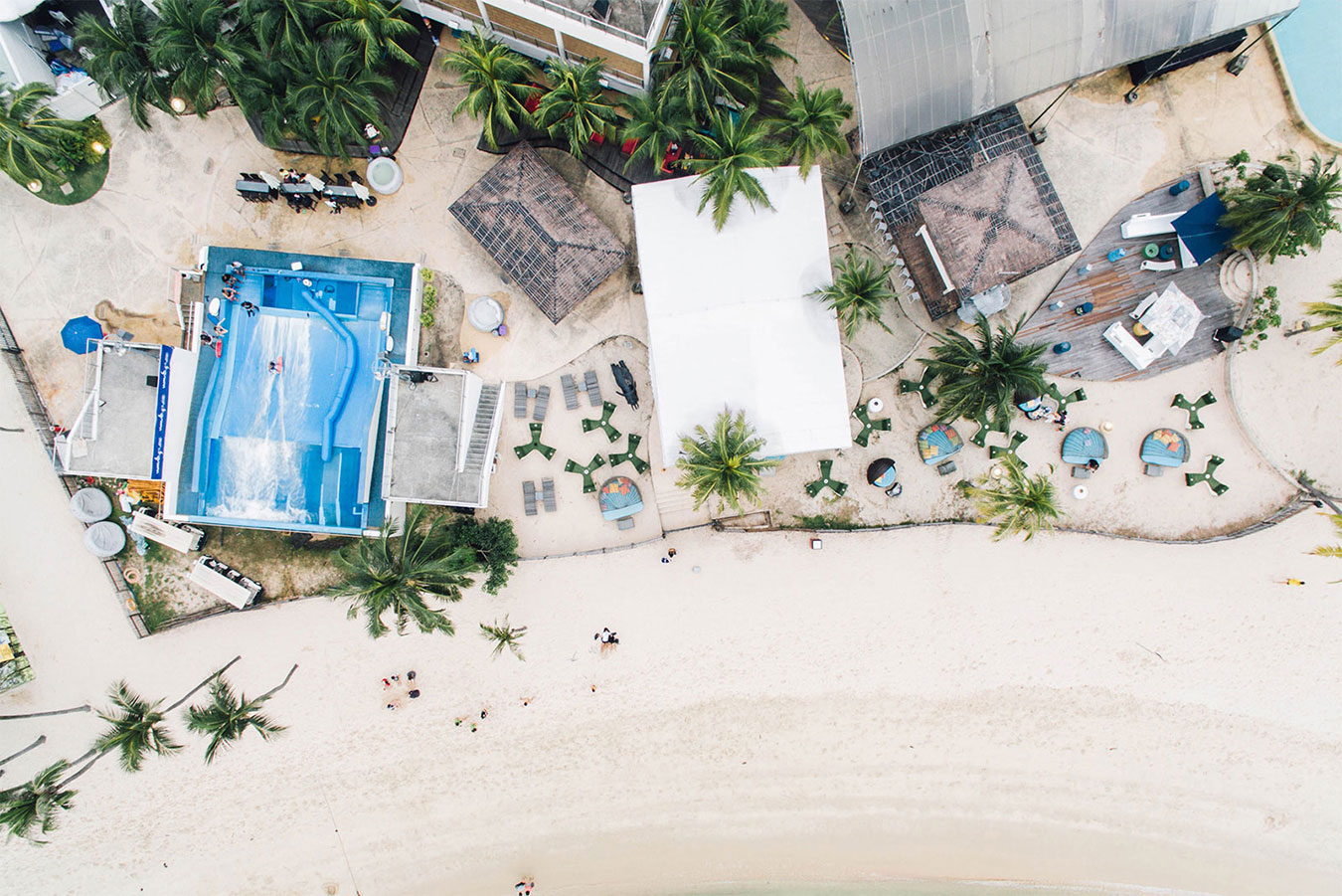 Vue aérienne d'une station balnéaire avec piscine, plage de sable et palmiers sous climat tropical